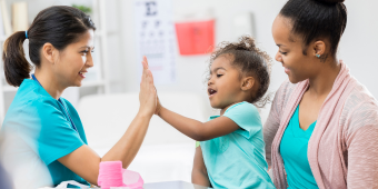Photo of a child with their parent high-fiving a doctor