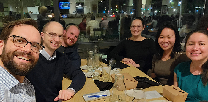 "Six scholars pose for a group photo at a table in a restaurant"