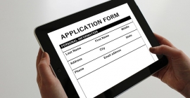 "Hands holding an iPad with a screen showing an application form"