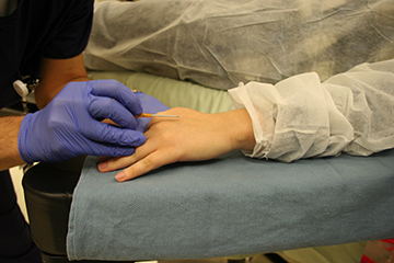 "Two hands, one of a gloved medical professional holding a tool, the other of a patient"