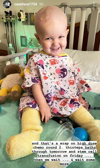 "A smiling baby sitting on a hospital bed"