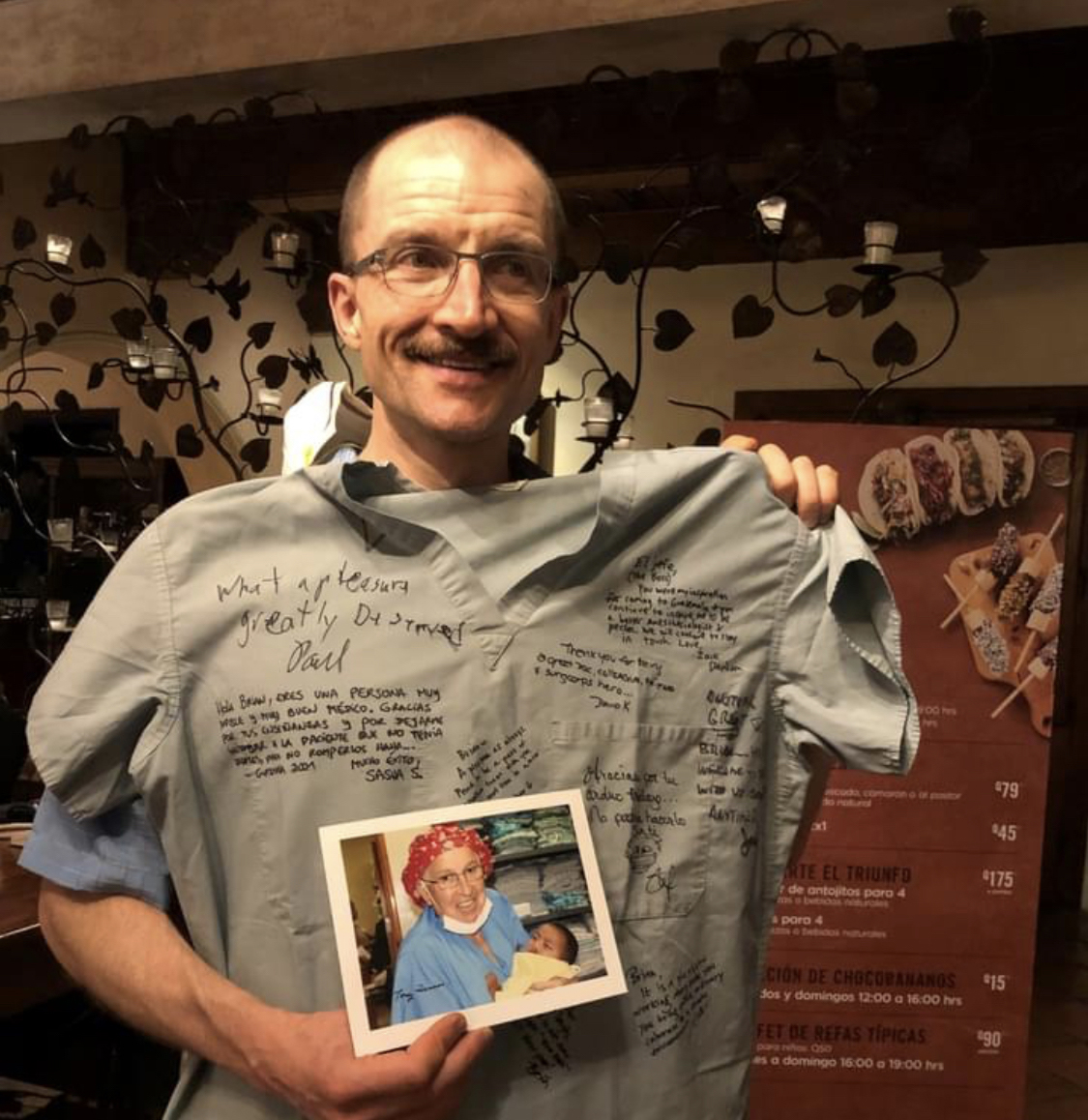 "Doctor Gierl posing with a signed scrub top and a photo of a nurse holding a baby"