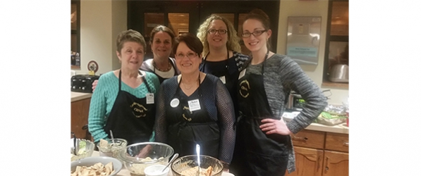 "Five CRNAs pose in front of a table with food"