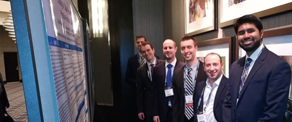 "A group of men in suits standing in front of a poster"