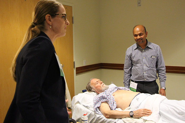 "Three people, one on laying on a hospital bed or gurney flanked by the two others, standing"