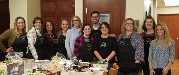 "A group of CRNAs in aprons posing behind a table full of food"