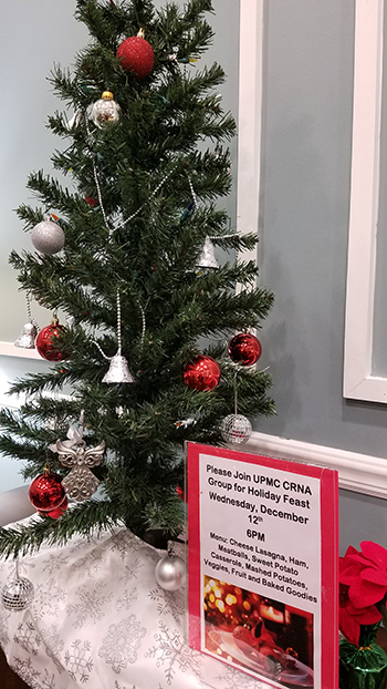"A small Christmas tree with red and silver ornaments along with an advertisement for the holiday dinner"