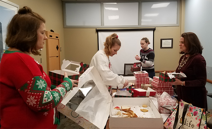 "CRNAs in holiday sweaters around a table with cookies and decorative boxes"
