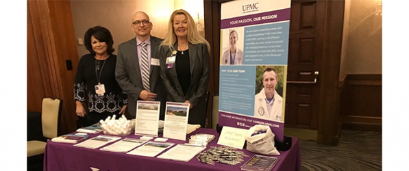 "Department members stand next to a poster at a table"