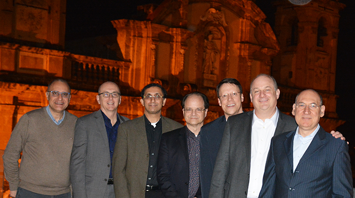 "Department Doctors pose as a group with a building lit in orange in the evening as the backdrop"