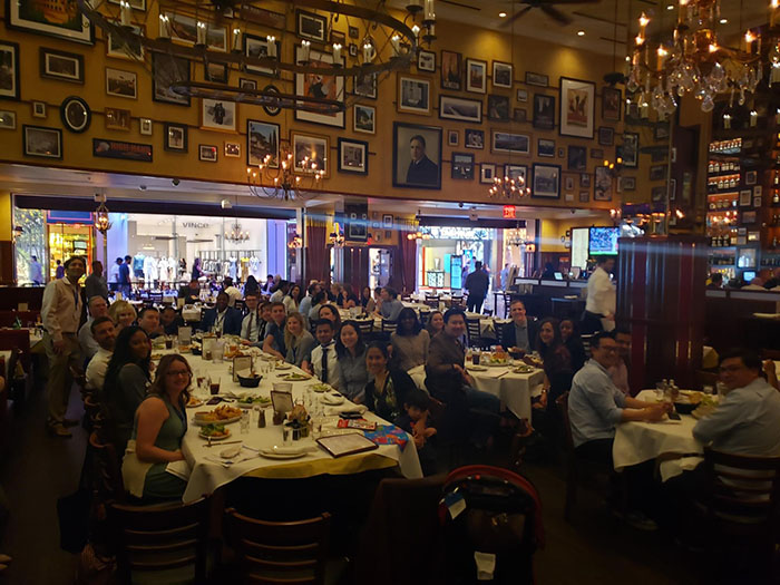 "Trainees sitting at many tables in a restaurant all smiling at camera"