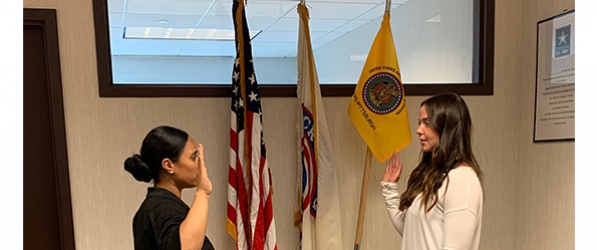 "Paige Tejera taking oath, hand raised, in front of flags"