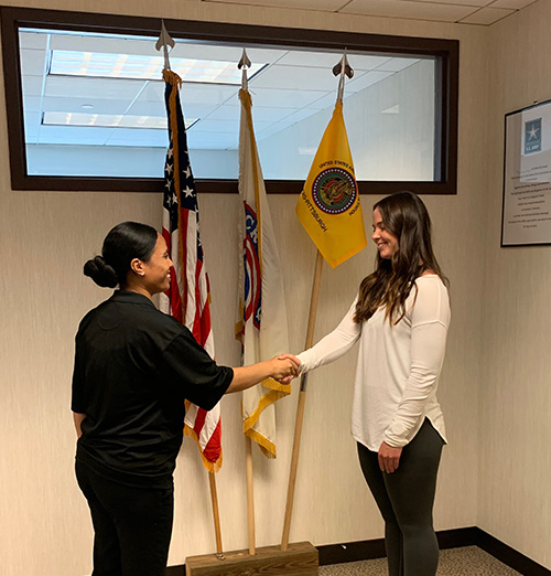 "Paige Tejera shaking hands with another woman in front of three flags"