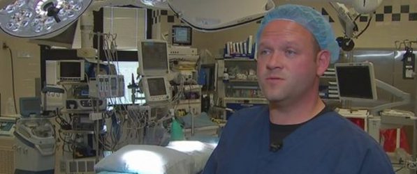 "A screenshot of Brett Fadgen from the news. Fadgen is in scrubs with a backdrop of medical equipment."
