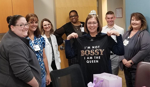 "A group of staff surrounding Laura who is holding a shirt that says I'm not bossy I am the queen"