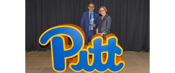 "Doctor Wasan stands with Provost Ann Cudd behind a waist-high Pitt logo"