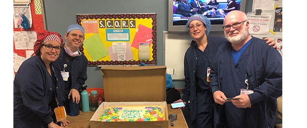 "CRNAs pose in front of a bulletin board next to a table with a cake"