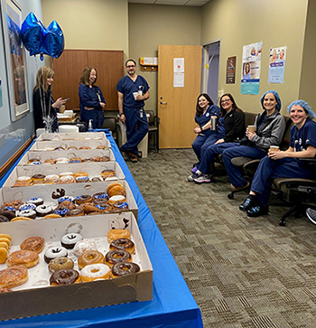 "CRNAs sit in a lounge, on the left is a table with many boxes full of donuts"