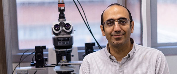 "Doctor Siamak next to a large medical microscope"