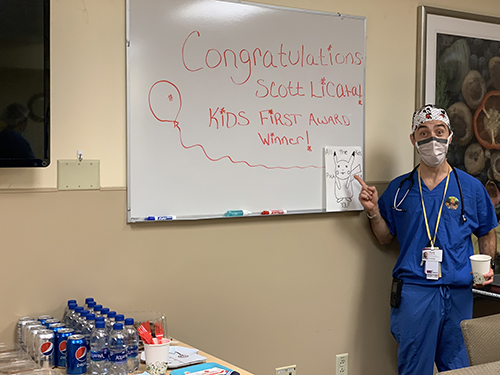 "Doctor Licata points at a white board with the text Congratulations Scott Licata Kids first award winner"