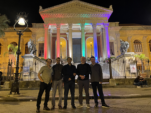 "Department members posing in front of a building at night with the pillars lit up in rainbow colors"