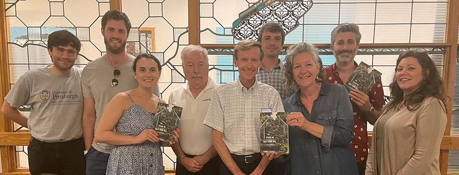 "Doctor Orebaugh poses with a group of department members holding his book titled The Stairs on Billy Buck Hill"