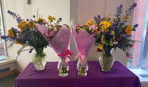 "Four bouquets of flowers in glass vases on a purple topped table"