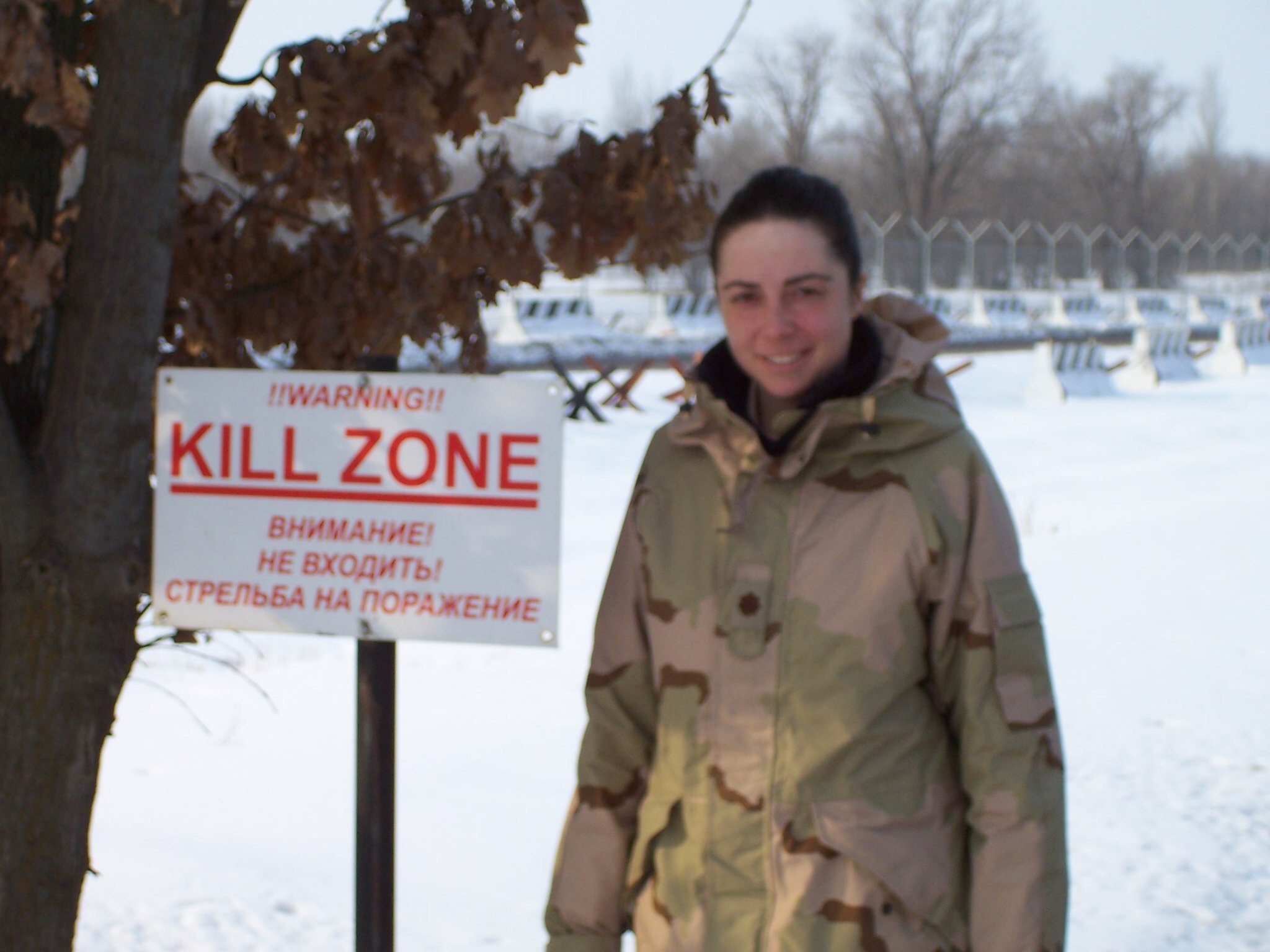 "An older photo of Wiggins in a camo coat standing next to a warning sign in the Winter"