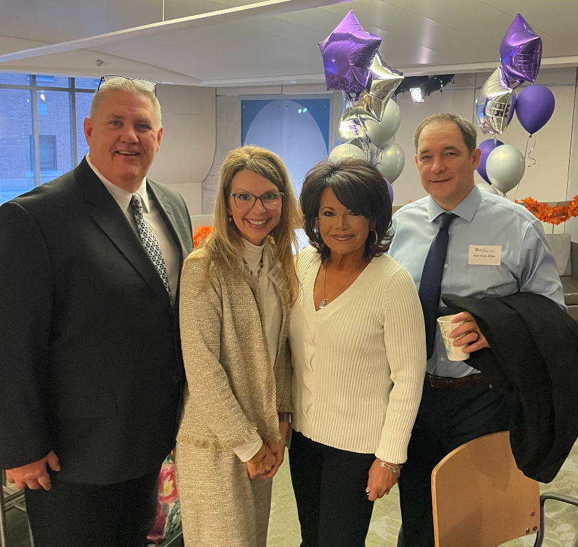 "Department members pose in a group for a photo with purple and silver balloons in the background"