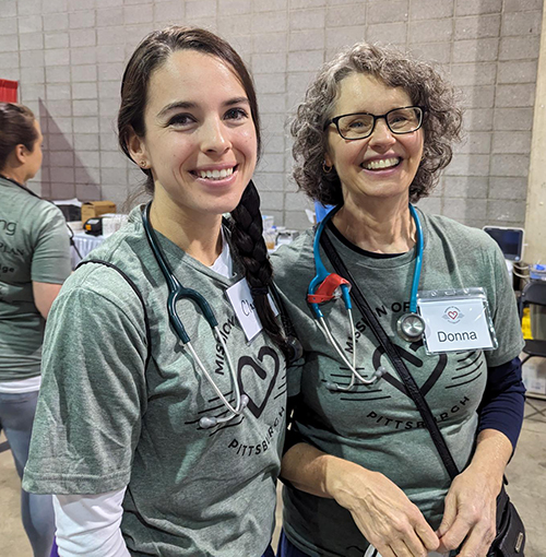 "Two department members pose for a photo in Mission of Mercy shirts and stethoscopes"