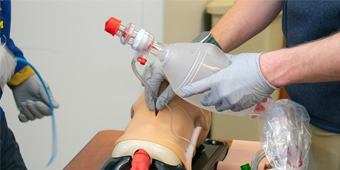 Closeup of the hands of a person wearing scrubs using a bagmask on a training mannequin