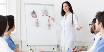 a woman points to an anatomical image of a heart before an audience of four trainees