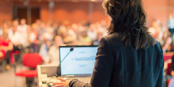 presenter at a laptop in front of attendee crowd