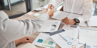 Two people shaking hands over a table full of manual papers