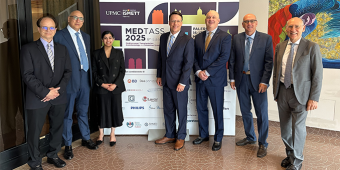 Seven professionally dressed individuals stand together in front of a banner for the 8th Edition of MEDTASS 2025 (Mediterranean Transplantation Anesthesiology and Simulation Symposium) held in Palermo. The banner features the UPMC and ISMETT logos, event dates (May 16–17, 2025), and logos of sponsoring organizations. The group poses in a hallway with tiled flooring and colorful artwork visible on the wall to the right.