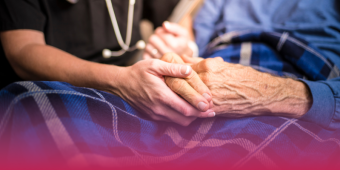younger healthcare worker holding the hands of an elderly patient