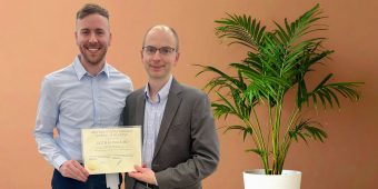 Two men stand side by side smiling; both are dressed in business casual attire. Taylor Duffy is on the left, and on the right is Keith M. Vogt, MD, holding an award certificate from the University of Pittsburgh School of Medicine.